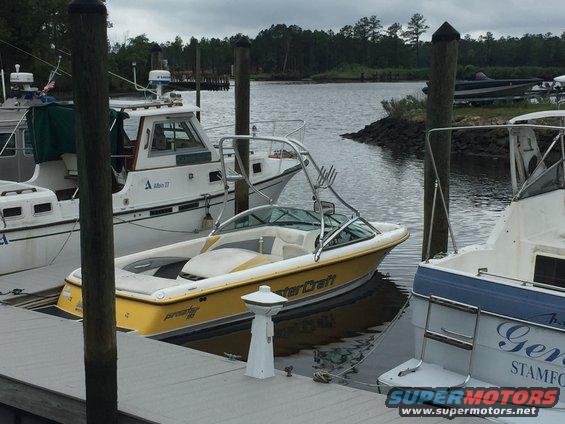 Yellow Mastercraft boat with wakeboard tower docked in a marina next to other boats
