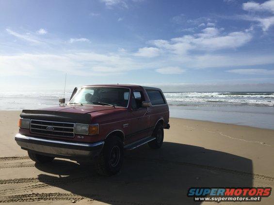1991 Ford Bronco parked on a beach with the ocean in the background