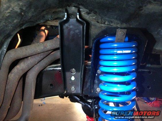 Blue coil spring and rusty exhaust manifold attached to black suspension components