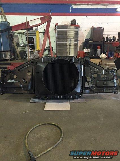 Radiator and front clip assembly removed from a vehicle, resting on the floor of a garage
