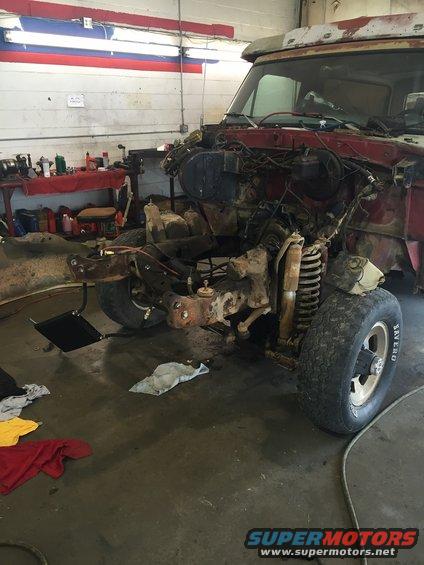 Truck front end disassembled in a garage, engine bay empty, suspension parts visible