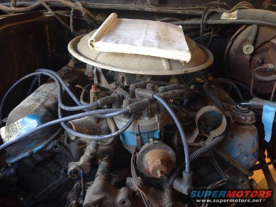 Engine bay with a manual on the air cleaner, showing distributor, spark plug wires, and engine block
