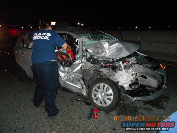 Silver sedan with severe front-end damage, emergency personnel attending