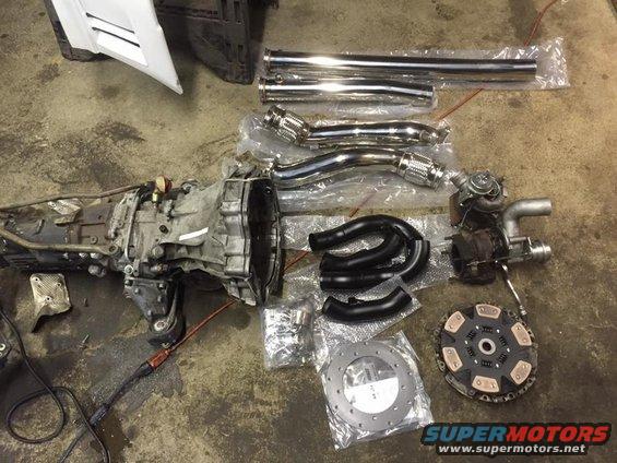 Transmission, turbo, exhaust pipes, and clutch parts are spread out on a concrete floor
