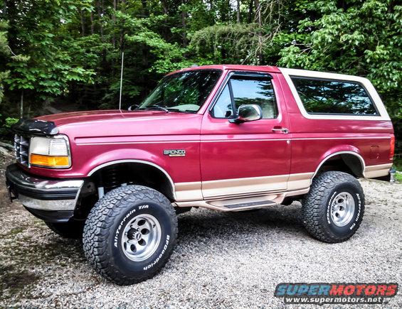 Red Ford Bronco with tan trim and off-road tires parked on gravel