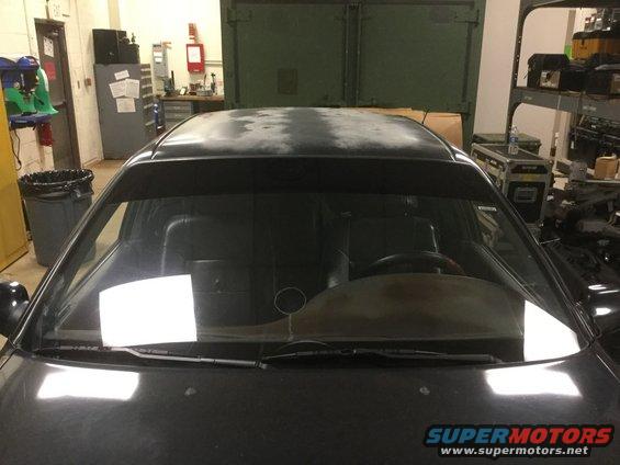 Black car interior seen through windshield, dashboard and steering wheel visible. Wipers on glass