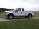 2011 Ford F-250 - This white 2011 Ford F-250 Super Duty pickup truck is shown from the side, parked on a gravel driveway.