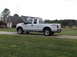2011 Ford F-250 - A white Ford F-250 Super Duty pickup truck is parked on a gravel driveway near a house and trees.