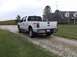 2011 Ford F-250 - This white 2011 Ford F-250 Super Duty pickup truck is seen from the rear 3/4 angle on a gravel driveway.