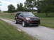2016 Ford Explorer - A brown 2016 Ford Explorer is parked on a gravel driveway surrounded by grass and trees.