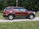 2016 Ford Explorer - A maroon 2016 Ford Explorer is shown from the side, parked on a gravel driveway with grass and trees in the background.