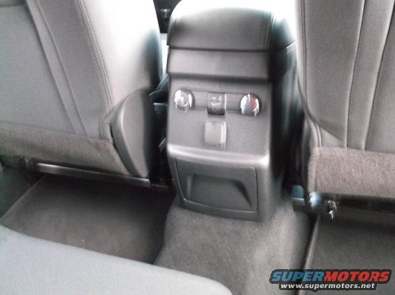 Center console with power outlets and climate controls between rear seats of a vehicle