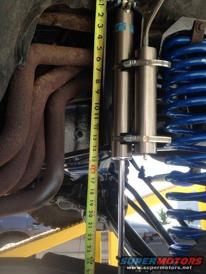 Suspension components including exhaust manifold, blue coil spring, and shock absorber, with a tape measure for scale