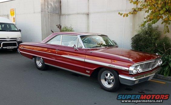 Red 1964 Ford Galaxie 500 coupe with chrome trim and aftermarket wheels, parked next to a white van