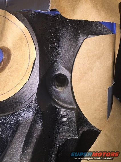 Close-up of a black engine part with masking tape covering some areas. There's a threaded hole visible