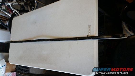 Black metal trim piece with visible mounting holes, resting on a white folding table
