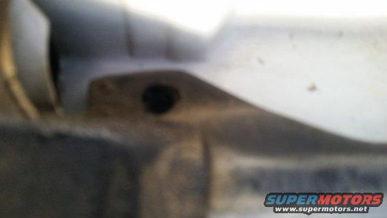 Close-up of a light-colored vehicle body panel with a dark hole and some dirt