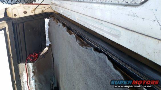 Interior view of a vehicle showing torn upholstery near the rear opening, with red wiring visible