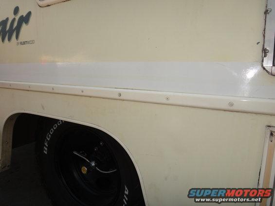 Cream-colored motorhome side panel with a white stripe above the wheel well. BFGoodrich tire visible