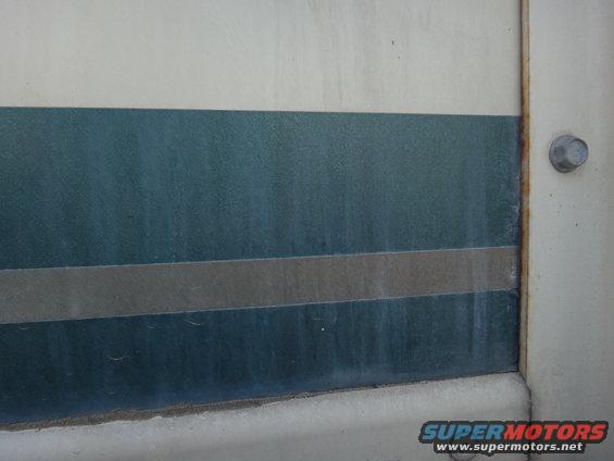 Side panel of a vehicle with horizontal teal and gray stripes. A bolt is visible on the right
