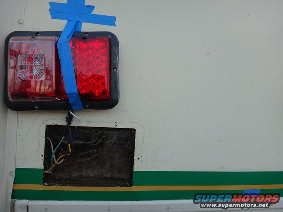 Tail lights taped to a white vehicle side with exposed wiring below