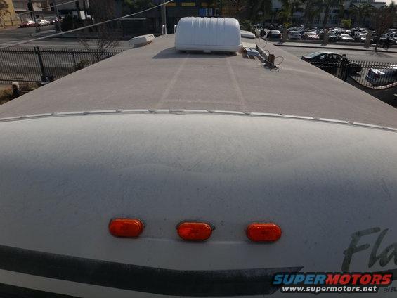 Top view of an RV roof showing three orange marker lights and a white roof unit
