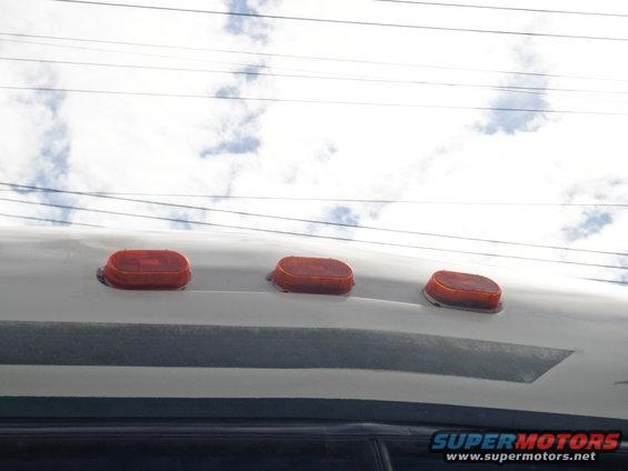 Three orange oval marker lights on the roof of a vehicle against a cloudy sky