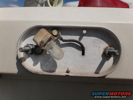 Close-up of a vehicle tail light assembly showing a bulb, wiring, and mounting hardware. Text reads 'DOT P2 85'