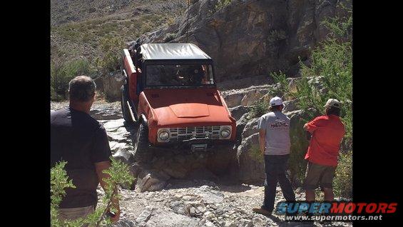Orange off-road vehicle with a white soft top navigating a rocky trail, front view