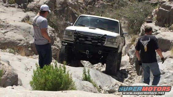White Ford Bronco navigating rocky terrain with two men nearby