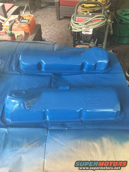 Two blue Ford valve covers, one with an embossed Ford logo, on a blue tarp