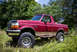 1995 Ford Bronco - This red 1995 Ford Bronco features a two-tone paint scheme and a removable top, captured in a natural outdoor setting.