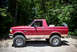 1995 Ford Bronco - This red Ford Bronco is parked outdoors with trees in the background. It has a spare tire in the cargo area.