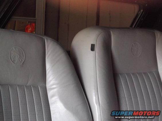 Close-up of light gray leather car seats with embossed circular emblems