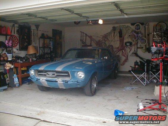Blue 1967 Ford Mustang with silver stripes parked in a garage, front view