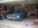 1967 Ford Mustang - A blue 1967 Ford Mustang with silver racing stripes is parked inside a garage.