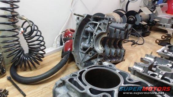 Engine block and cylinder head parts on a workbench with an air hose and grinders in the background
