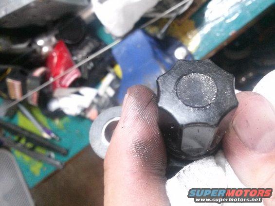 Hand holding a black, star-shaped knob with a silver circular insert. A roll of gray tape is also visible