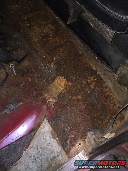 rusted floor pan inside a vehicle, showing significant corrosion and damage