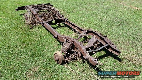 rusted vehicle frame lying on grass, covered in weeds