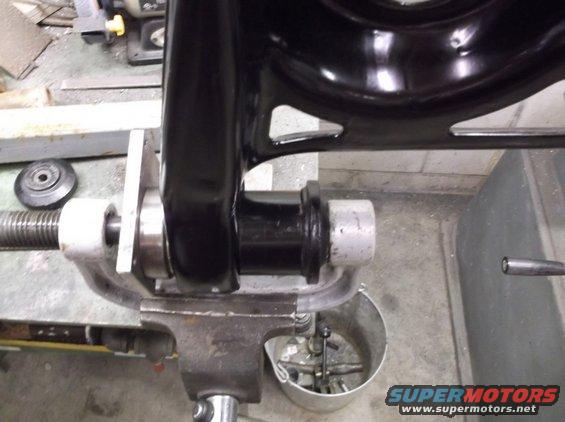 Black metal suspension component clamped in a vise with a threaded rod