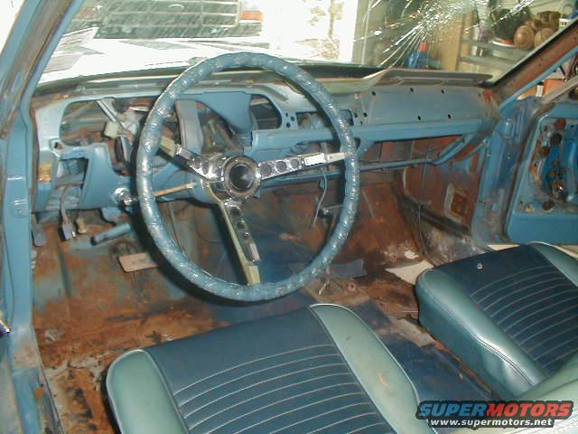 1967 Ford Mustang interior with blue dashboard, cracked windshield, and rusty floor pans