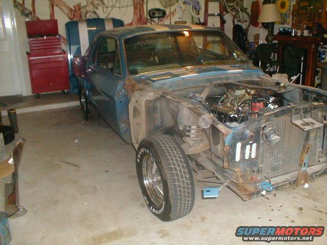Blue 1960s Ford Mustang with racing stripes, front end removed, engine exposed, in a garage