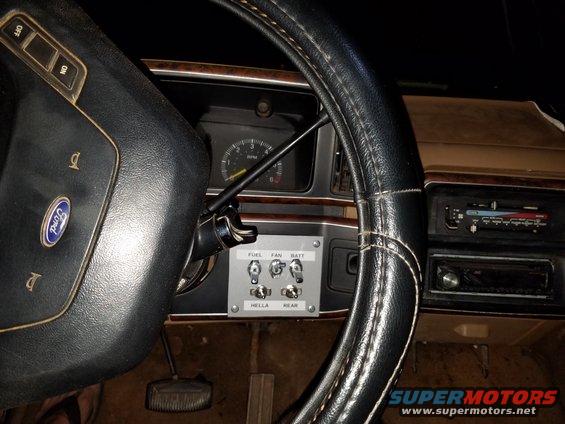 Interior shot of a vehicle's dashboard, showing a steering wheel, instrument cluster, and a panel with aftermarket switches labeled FUEL, FAN, BATT, HELLA, and REAR