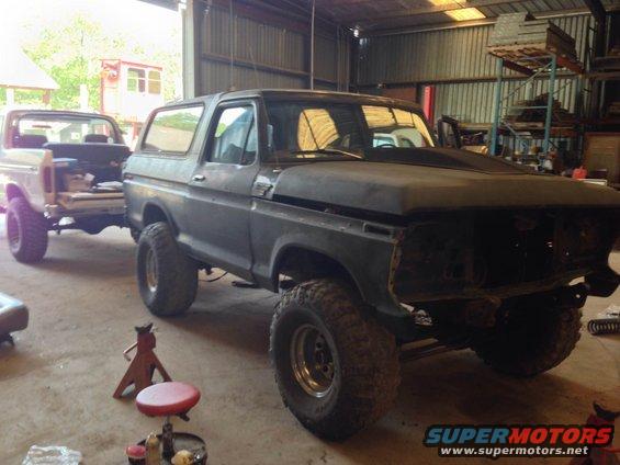 1979 Ford Bronco in a garage with hood open, next to a white pickup truck.