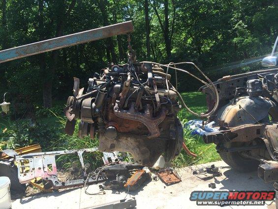Engine being lifted by a hoist, with parts of a car chassis visible