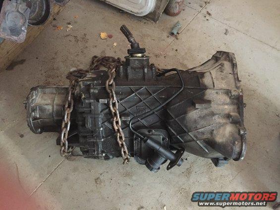Dirty transmission with a chain wrapped around it, resting on a concrete floor