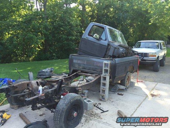 Disassembled truck chassis with cab in bed, white SUV in background