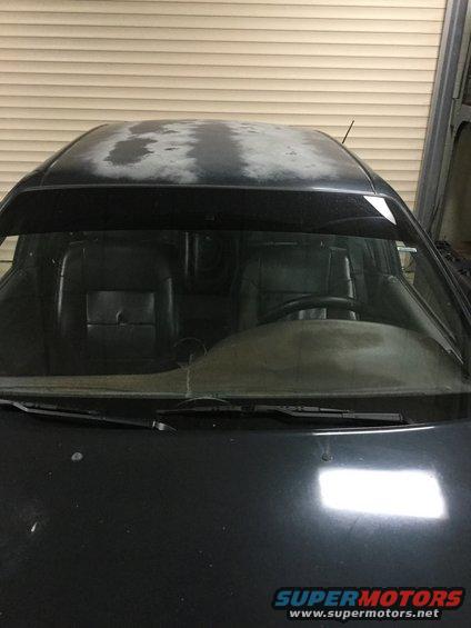 Black car interior with worn seats and steering wheel, viewed through the windshield. Faded paint on the roof