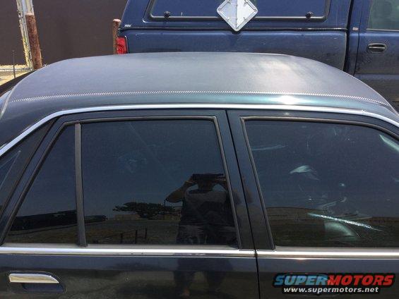 Side view of a dark sedan with tinted windows, a blue pickup truck is behind it